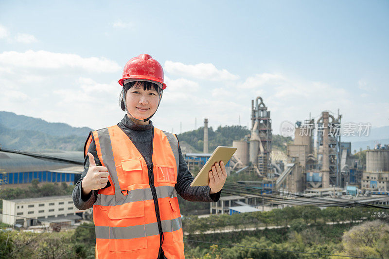 A female engineer uses a tablet computer in a cement plant and thumbs up